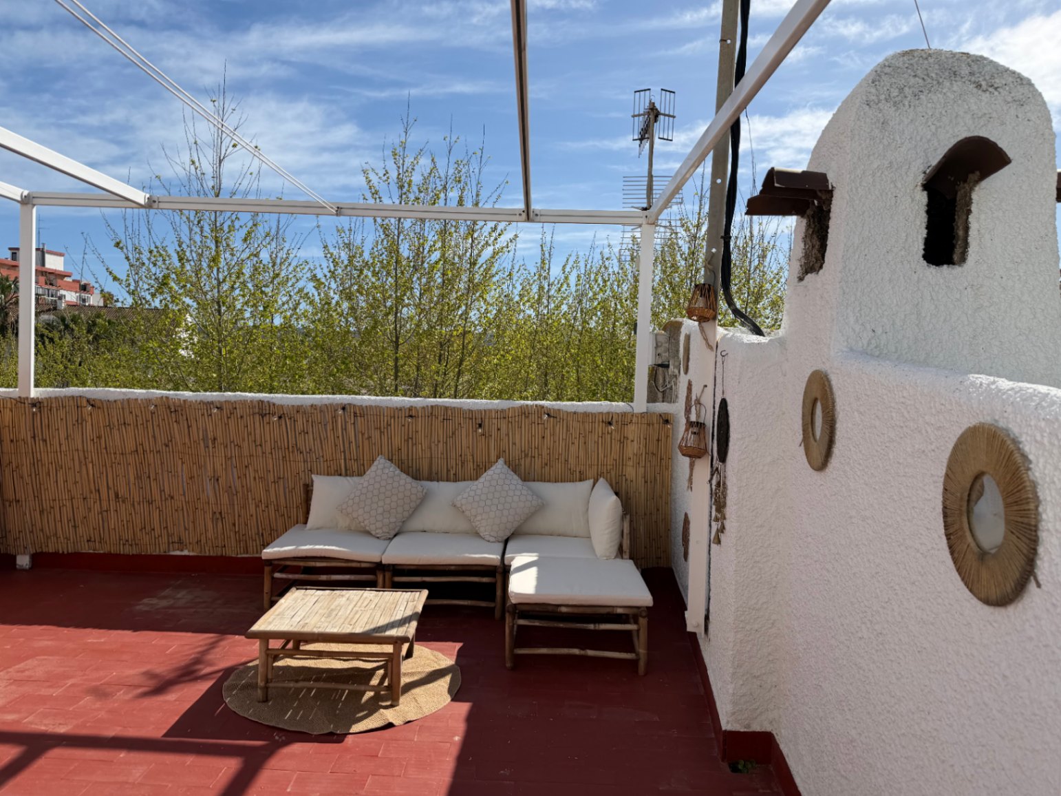 Terrasse mit rotem Boden, dekorierter weißer Wand, Bambussofa und Blick auf das Grün.