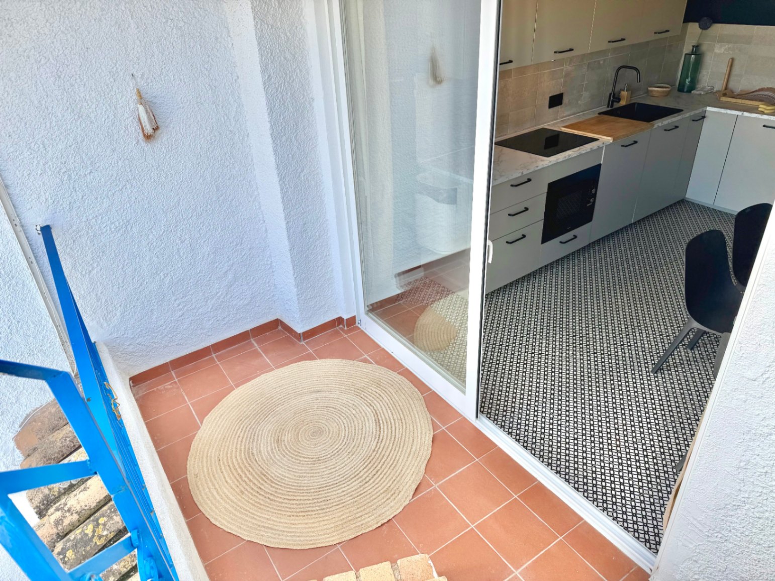 Terrasse mit Terrakottaboden und Zugang zu einer modernen Küche mit schwarz-weißem geometrischen Boden.