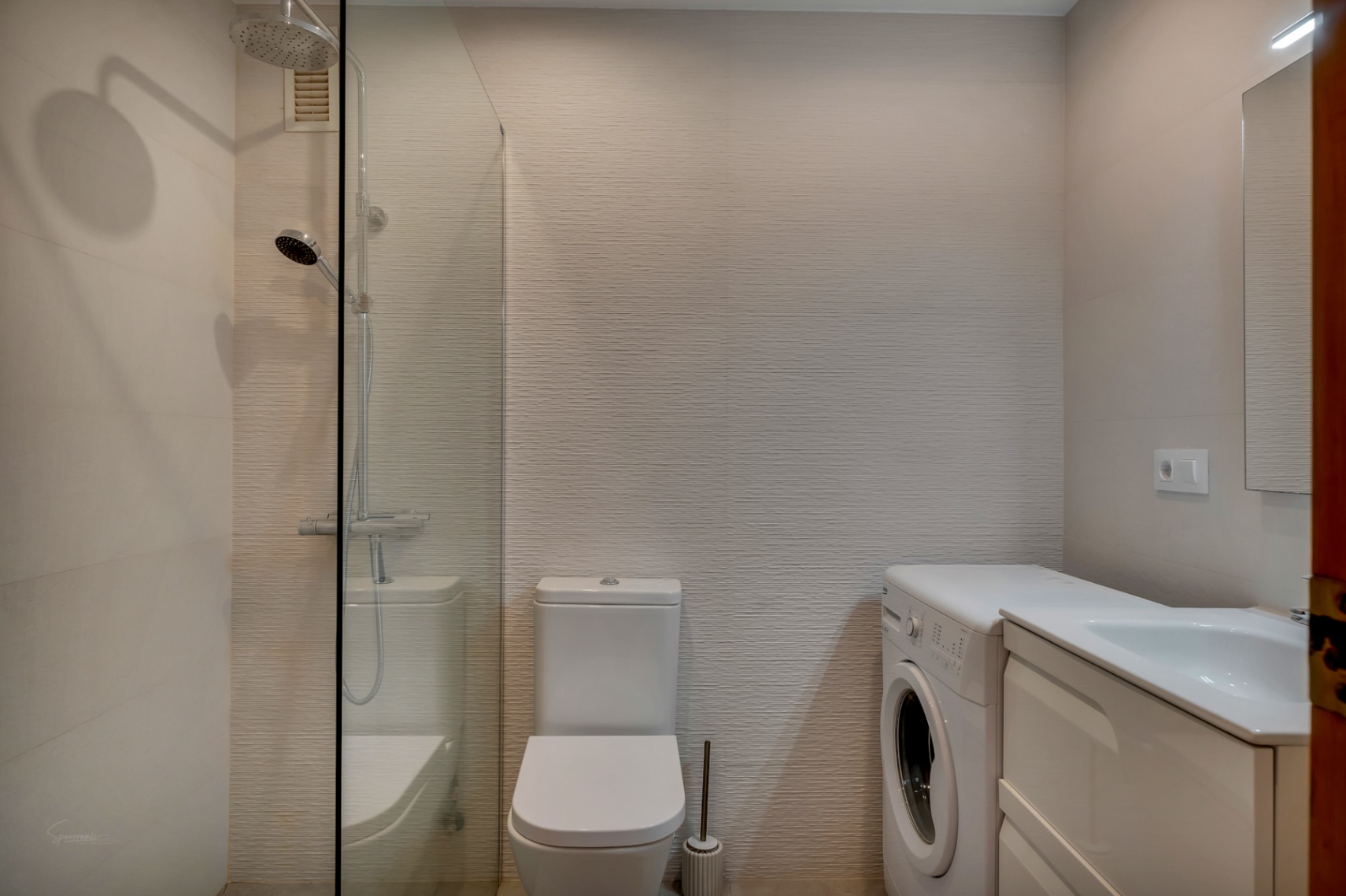 Badezimmer mit Glasdusche, weißer Toilette, Waschmaschine und Waschtisch mit weißem Unterschrank.