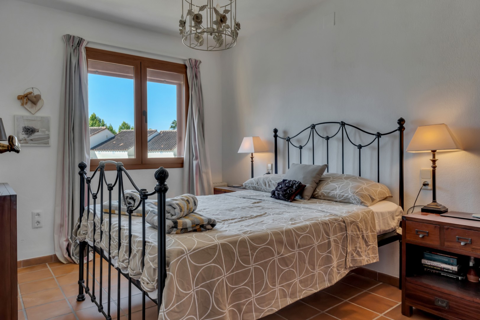 Helles Schlafzimmer mit Schmiedeeisenbett, Fenster mit Außenblick und Terrakottaboden.