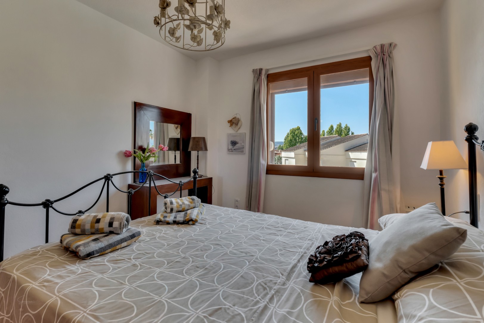 Helles Schlafzimmer mit schmiedeeisernem Bett, dunklem Holzwaschtisch und Fenster mit Außenansicht.