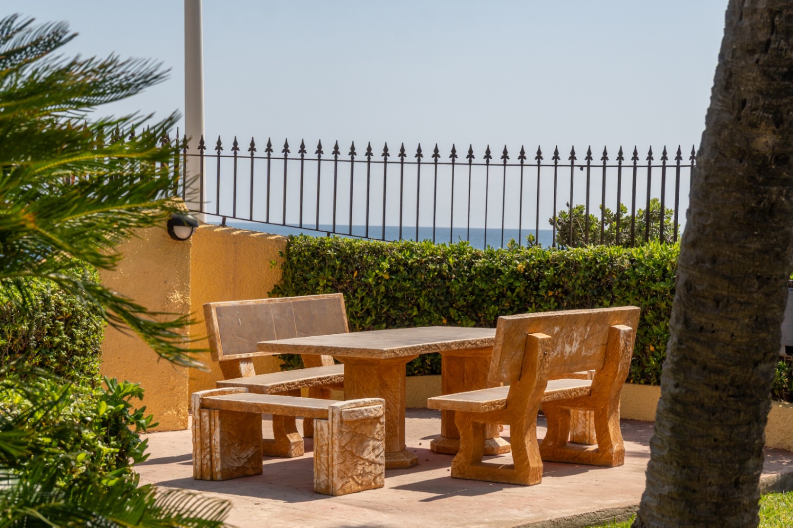 Sitzbereich im Freien mit Steintisch und Bänken, mediterranen Gärten und Meerblick.