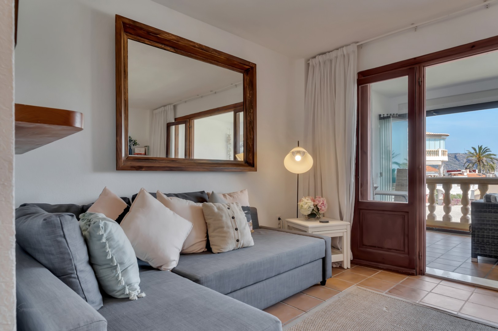 Wohnzimmer mit modularem grauen Sofa, Holzspiegel und Zugang zur Terrasse mit Aussicht.