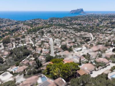 Luftaufnahme eines Küstenwohngebiets mit dem Mittelmeer und dem Peñón de Ifach in der Ferne, unter klarem blauem Himmel.