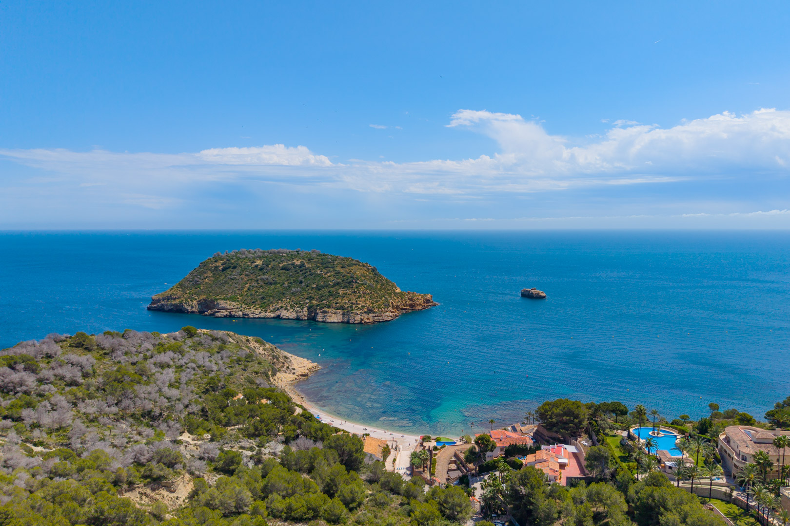 Luftaufnahme der Küste von Jávea mit Isla del Descubridor, Strand und Wohngebiet mit Pool.