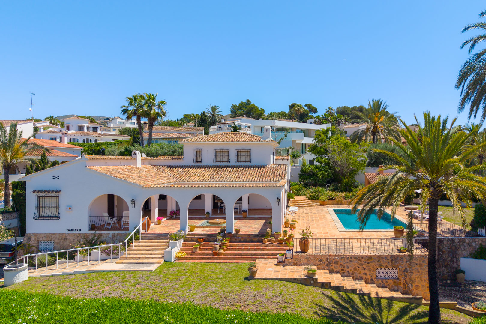 Erhöhte Ansicht der Villa mit Bögen, Pool und terrassenförmig angelegtem Garten mit Grün.