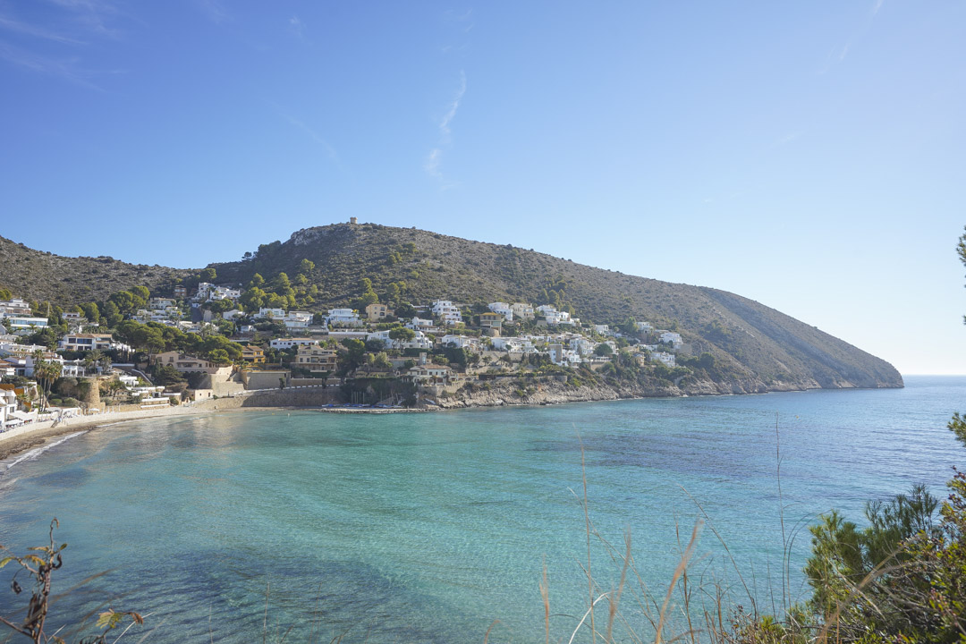 Panoramablick auf die Küste von Moraira mit türkisfarbenem Wasser und weißen Häusern am Hang.
