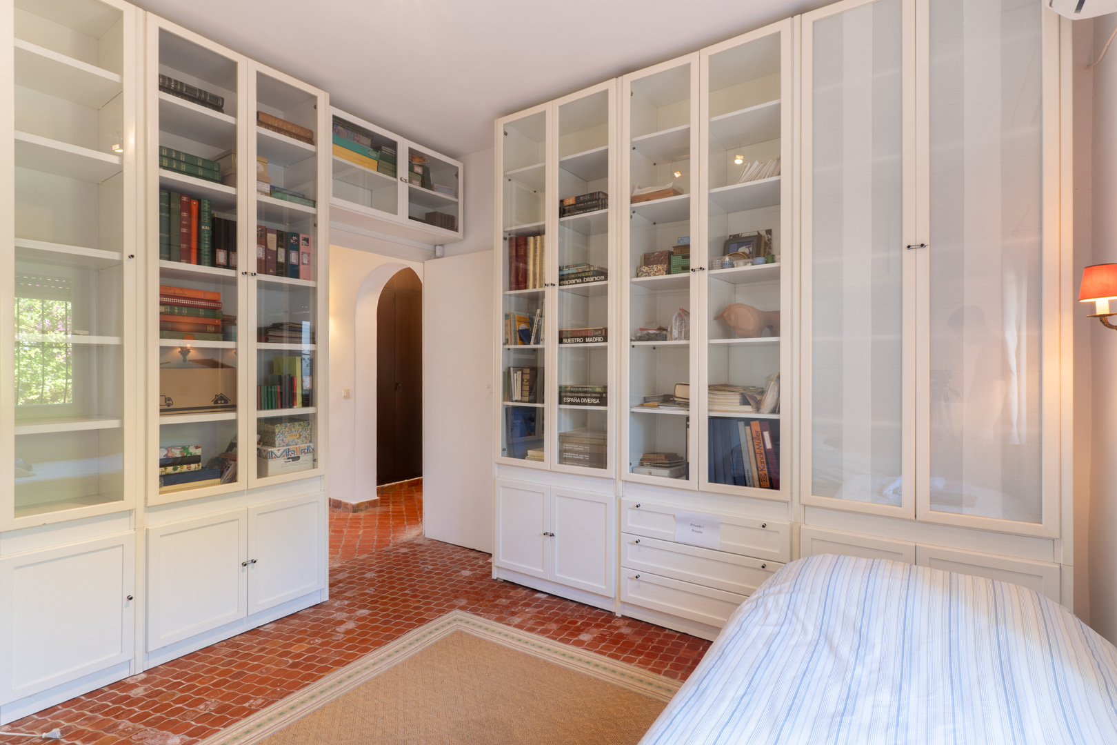 Schlafzimmer mit eingebauten weißen Regalen und Terrakottafliesenboden.