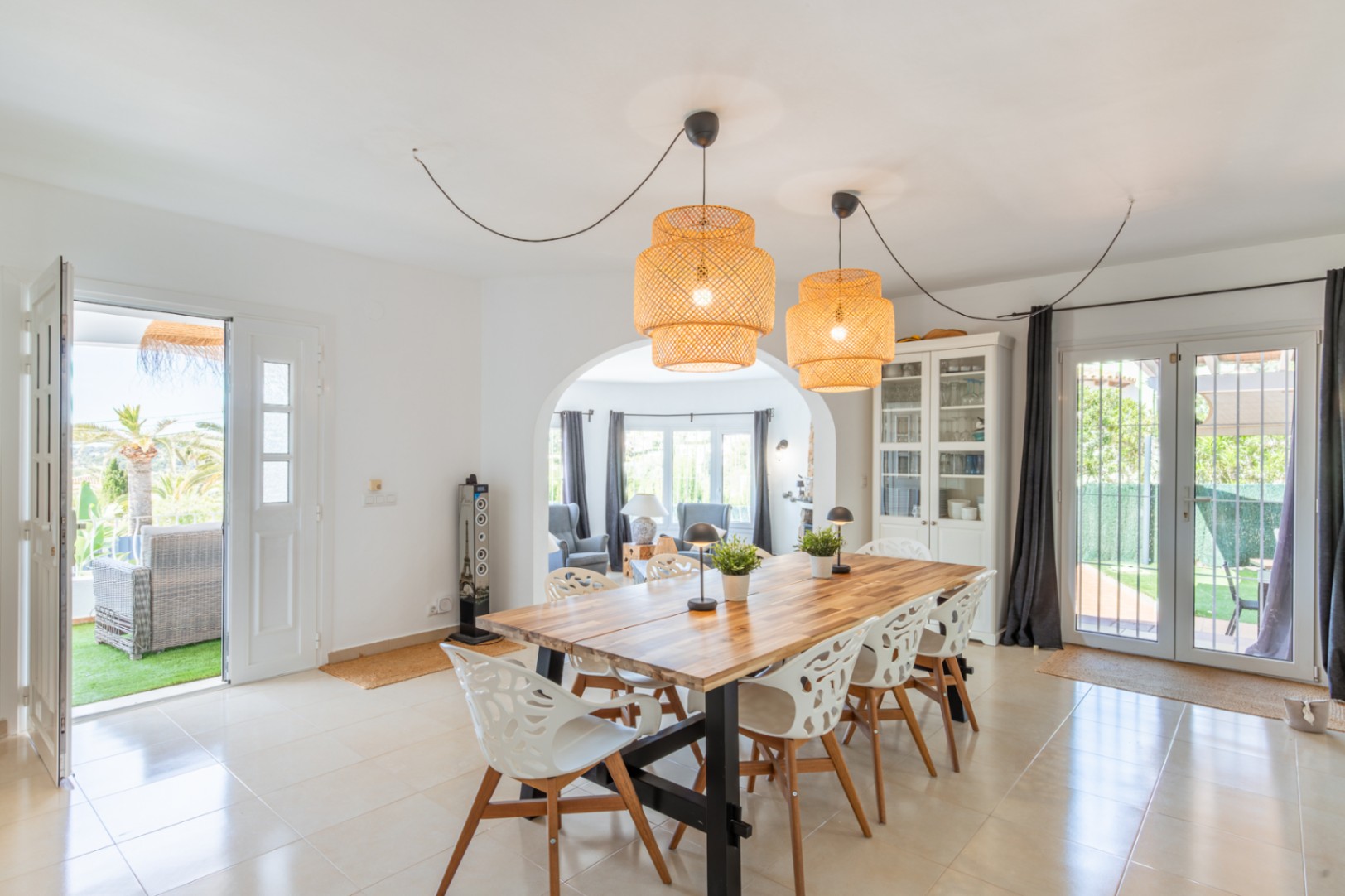 Heller Essbereich mit robustem Holztisch, markanten Rattan-Pendelleuchten und Fliesenboden. Er bietet direkten Zugang zur Terrasse und ist durch einen Bogen mit dem Wohnzimmer verbunden.