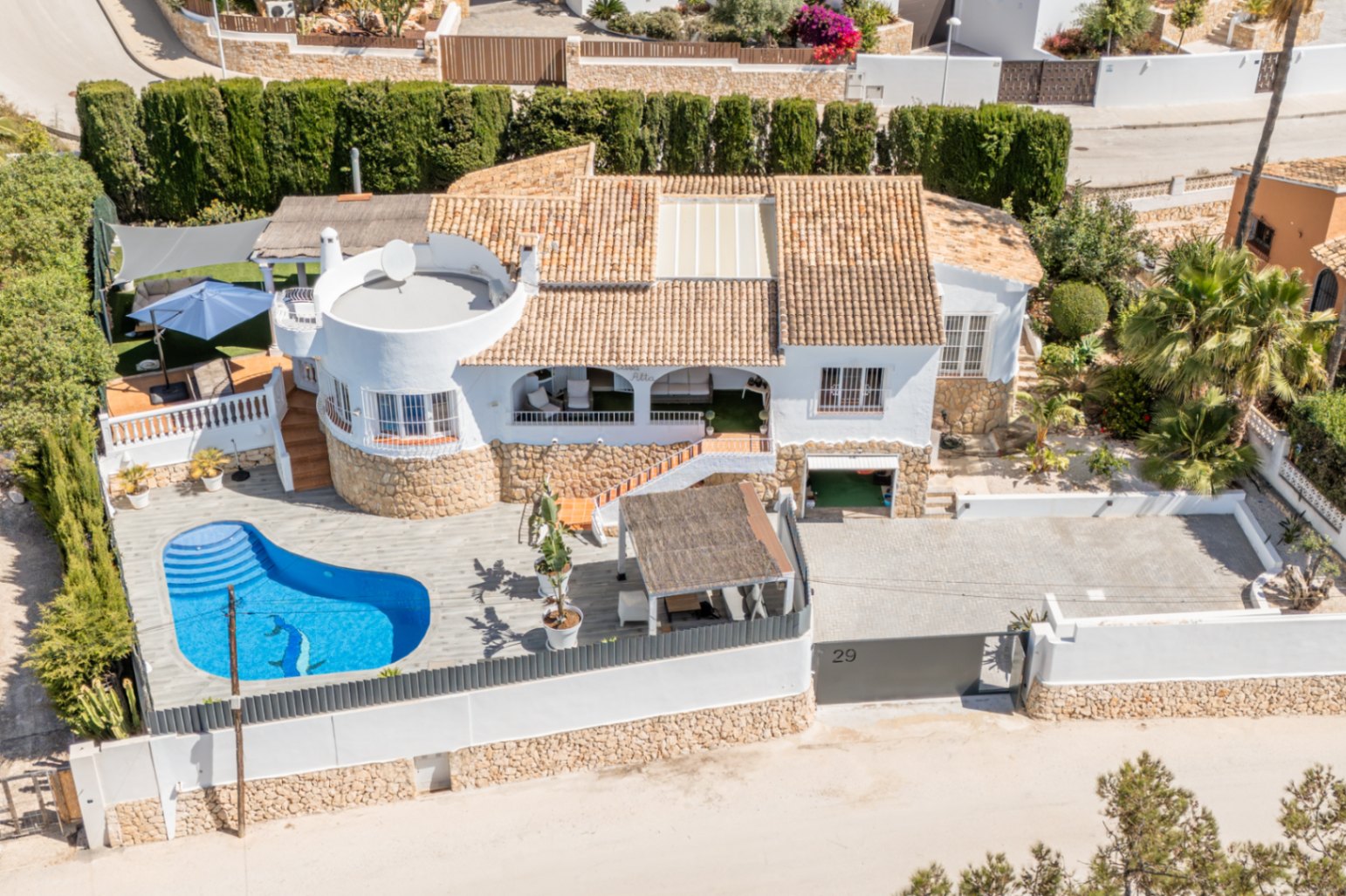Luftaufnahme der weißen Villa mit Terrakotta-Dach und nierenförmigem Privatpool mit Delfin-Mosaik. Die Immobilie bietet eine große gepflasterte Einfahrt und mehrere Außenterrassen.