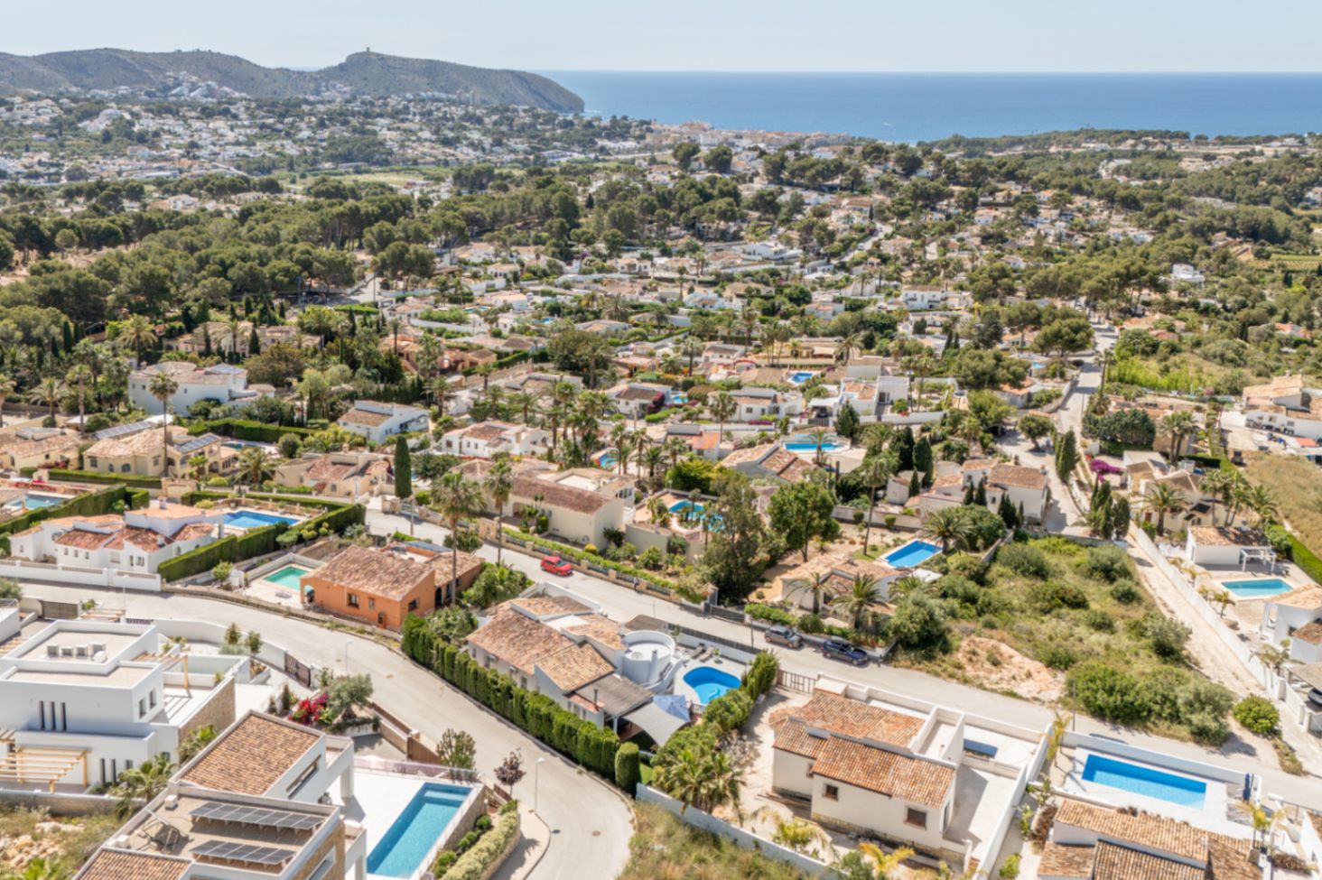 Luftaufnahme des Wohngebiets von Moraira, die die Dichte der Villen mit Ziegeldächern, privaten Pools und das blaue Mittelmeer am Horizont zeigt.