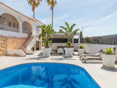 Außenansicht der Villa 'Casa Alta' mit blauem Mosaikpool. Die helle Holzterrasse umgibt den Pool, angrenzend an eine Außentreppe mit dekorativen Fliesen und Steinsockel.