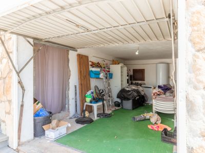 Garage oder Abstellraum mit Wellblechdach und grünem Kunstrasenboden. Enthält einen Warmwasserbereiter, Kühlschrank, Leiter und diverse Lagergegenstände.