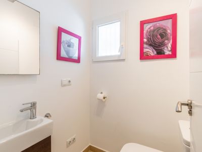 Gäste-WC mit rechteckigem Waschbecken, modernem Chromhahn und dunklem Holzwaschtisch. Ein kleines Fenster sorgt für Tageslicht, ergänzt durch Bilder mit pinken Rahmen.