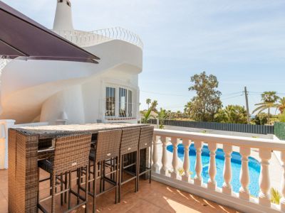 Geflieste Außenterrasse mit Rattan-Bartisch und Hockern, mit Blick auf den privaten Pool. Die weiße Villa zeigt ein einzigartiges spiralförmiges Architekturelement bei klarem Himmel.