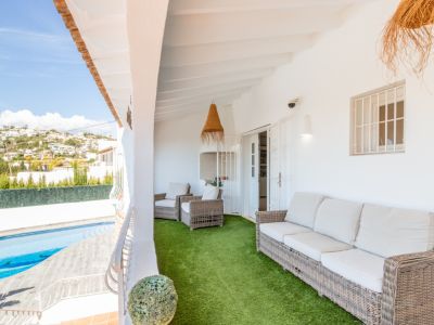 Geräumige überdachte Terrasse mit gemütlichen Korbmöbeln auf Kunstrasen, bietet Blick auf den privaten Pool und die bewachsenen Hügel in der Ferne.