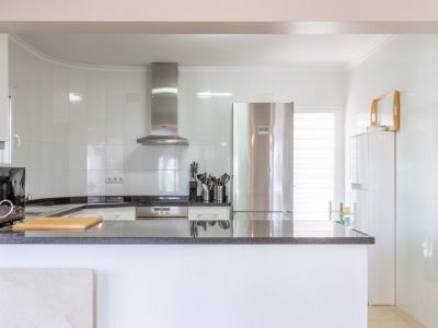 Helle, moderne Küche mit weißen Fliesenwänden, dunklen Granitarbeitsplatten und integrierten Edelstahlgeräten wie Kühlschrank und Dunstabzugshaube. Eine offene Theke bietet Arbeitsfläche.