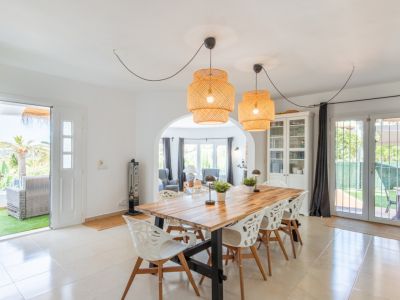 Heller Essbereich mit robustem Holztisch, markanten Rattan-Pendelleuchten und Fliesenboden. Er bietet direkten Zugang zur Terrasse und ist durch einen Bogen mit dem Wohnzimmer verbunden.