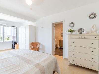 Helles Hauptschlafzimmer mit Doppelbett, weißem Kleiderschrank und direktem Zugang zum eigenen Bad. Das Fenster bietet Blick auf die Außenvegetation.