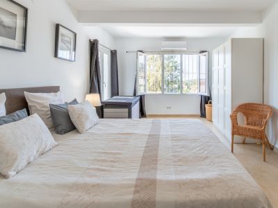 Helles Schlafzimmer mit großem Bett, hellen Fliesen, weißem Kleiderschrank und vergittertem Fenster mit Blick ins Grüne, inklusive Klimaanlage.
