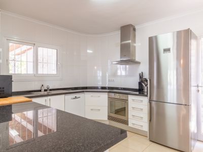Küche mit weißen Schränken, dunklen Granitarbeitsplatten und Edelstahlgeräten wie Kühlschrank und Einbaubackofen. Fenster mit Sicherheitsgittern bietet Tageslicht.