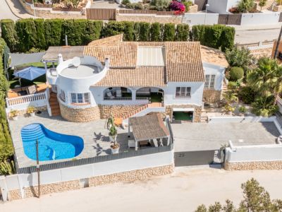 Luftaufnahme der weißen Villa mit Terrakotta-Dach und nierenförmigem Privatpool mit Delfin-Mosaik. Die Immobilie bietet eine große gepflasterte Einfahrt und mehrere Außenterrassen.