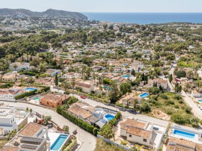 Luftaufnahme des Wohngebiets von Moraira, die die Dichte der Villen mit Ziegeldächern, privaten Pools und das blaue Mittelmeer am Horizont zeigt.