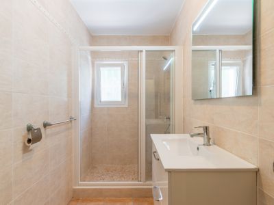 Modernes Badezimmer mit beigen Wandfliesen, weißem Waschtisch, LED-Spiegel und einer begehbaren Dusche mit Mosaikboden und Fenster.