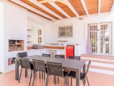 Überdachte Außenterrasse mit integriertem Grill, funktionaler Außenküche inklusive rotem Minikühlschrank und großem Esstisch. Der Bereich verfügt über Terrakottaboden und eine Lattenholzdecke.