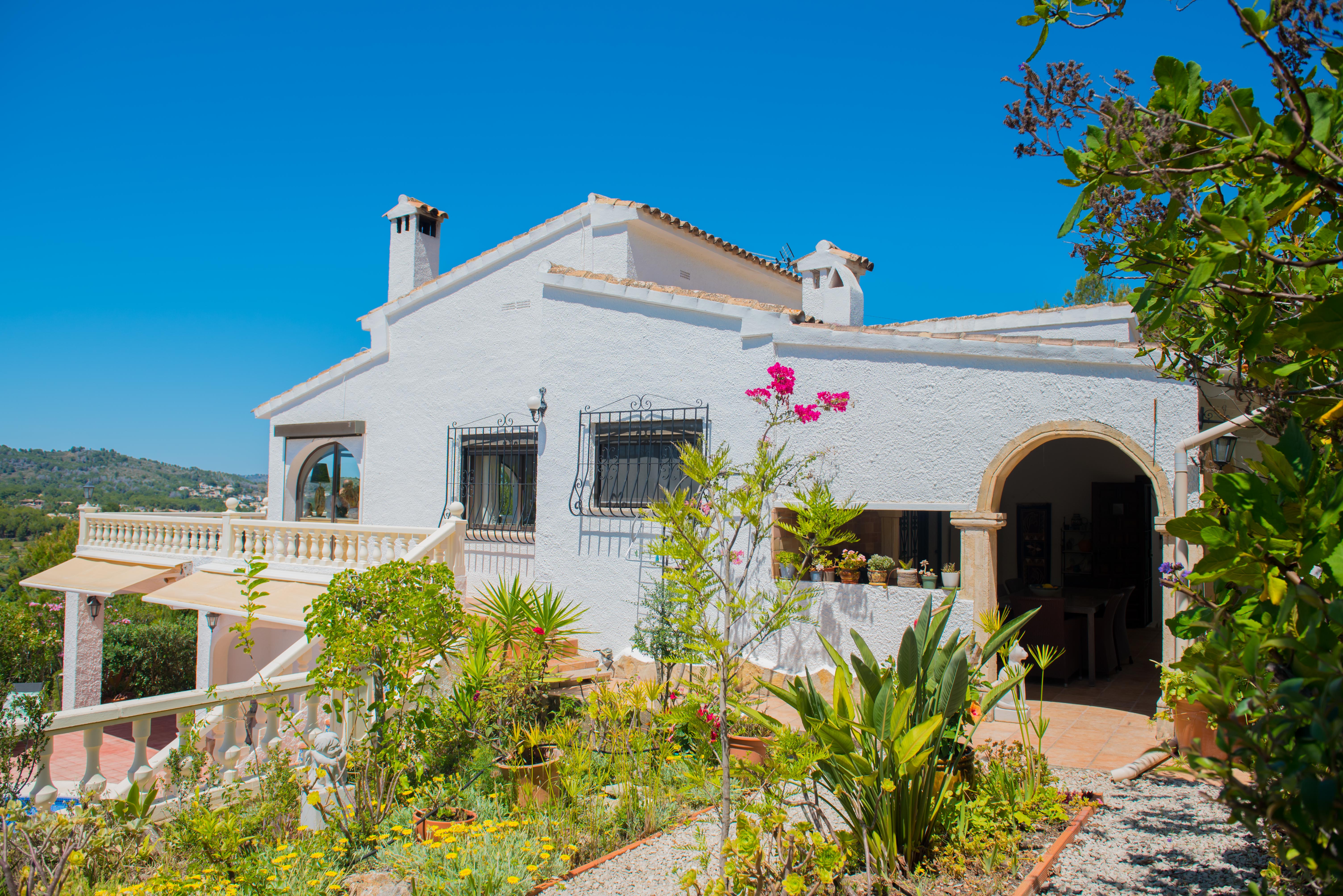 Außenansicht der mediterranen Villa mit Garten, strukturierten weißen Wänden und Balustraden-Balkonen.