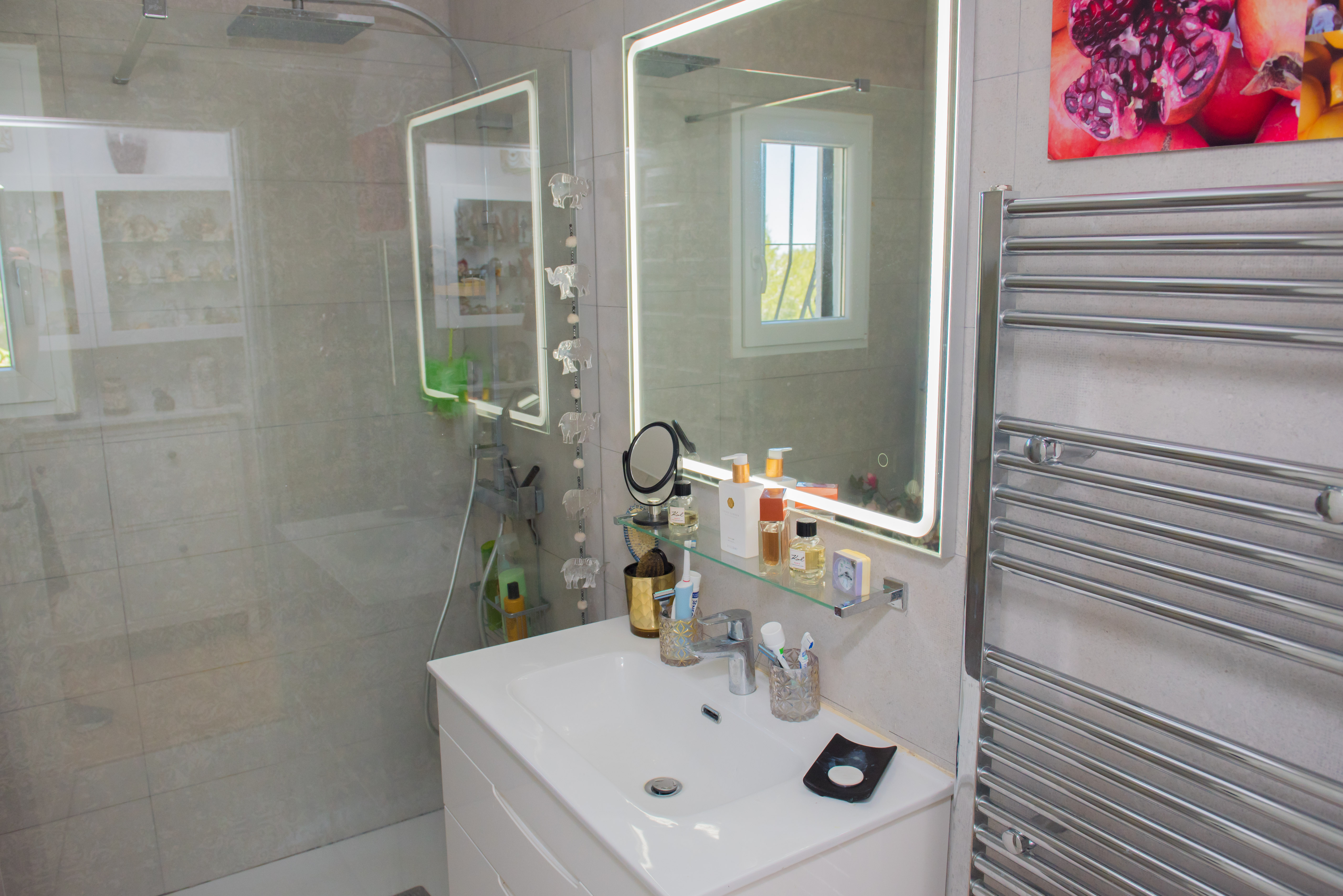 Badezimmerdetail mit weißem Waschbecken, beleuchtetem Spiegel und Chrom-Handtuchwärmer.