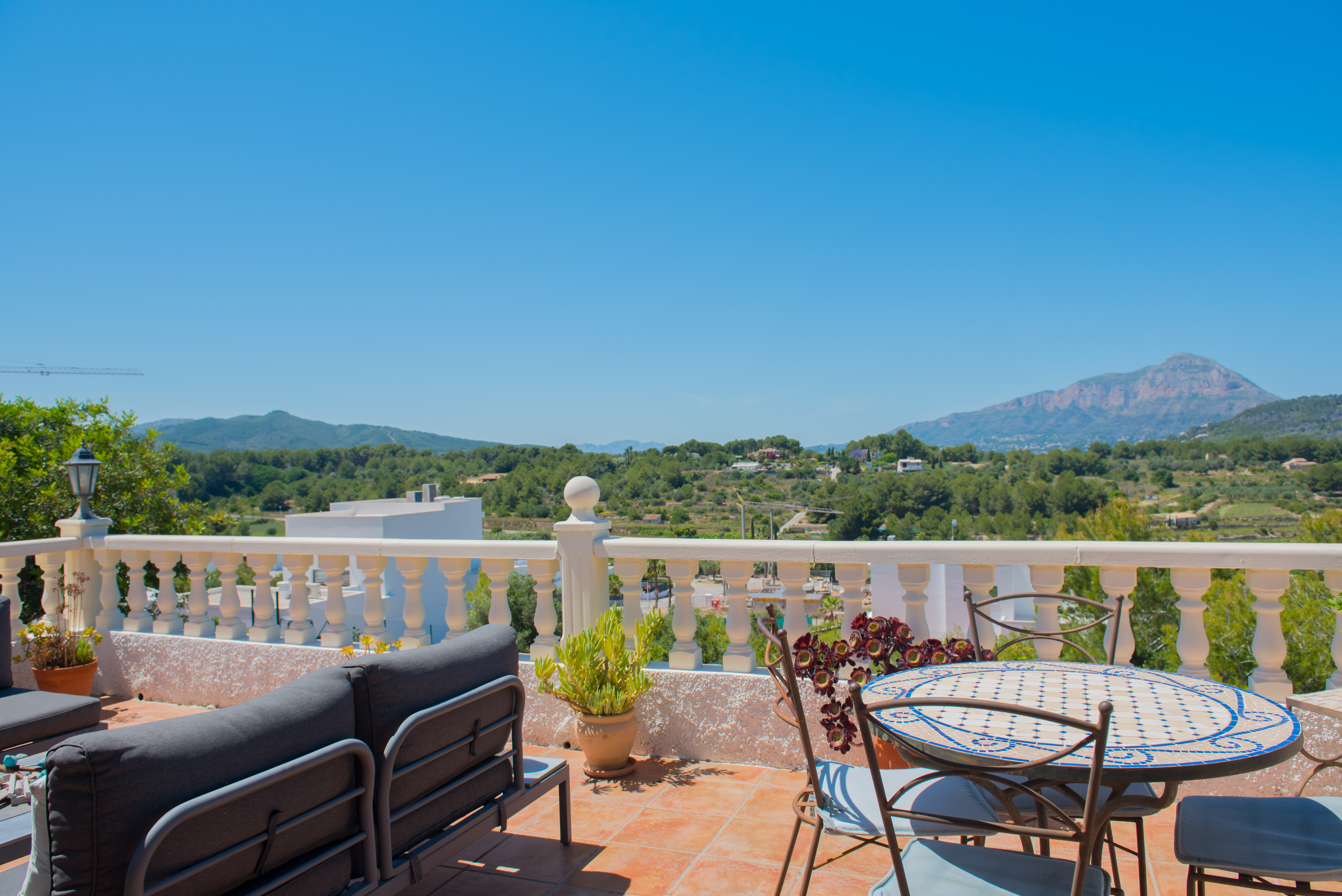 Geflieste Terrasse mit Bergblick, möbliert mit einem grauen Sofa und einem Mosaiktisch.