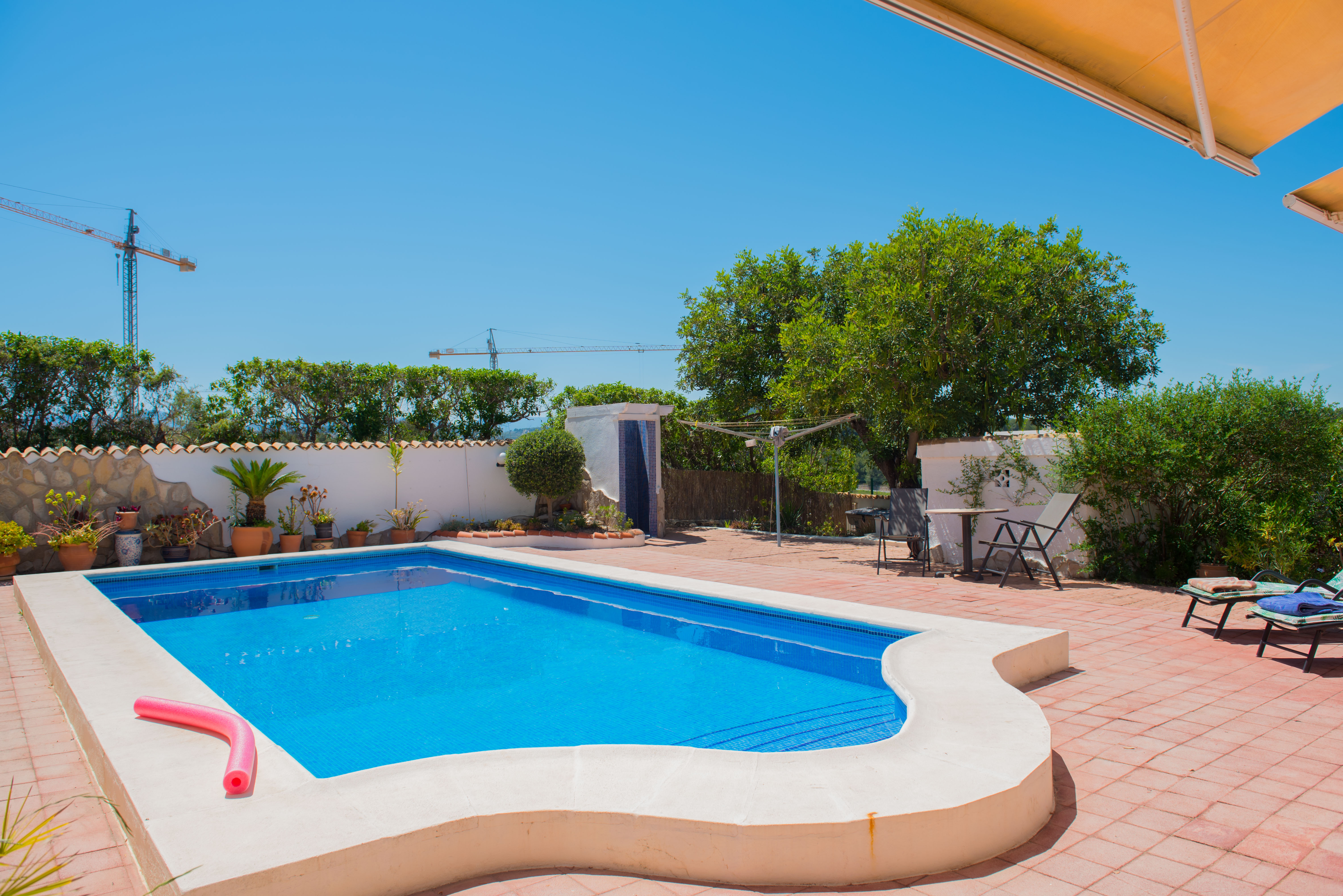 Pool mit blauen Mosaikfliesen und weißem Zementrand auf einer rot gefliesten Terrasse.
