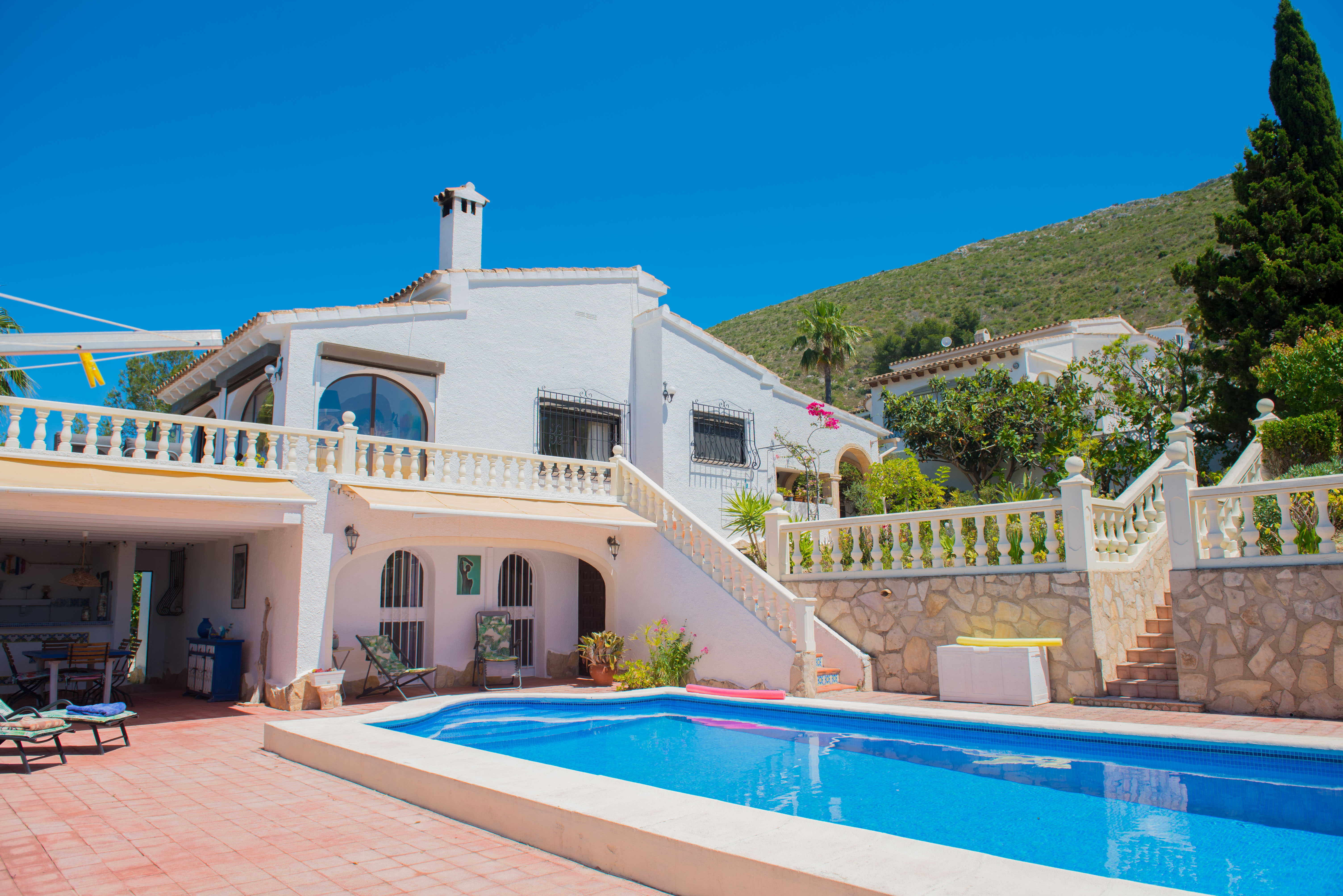 Poolblick mit roten Fliesen und weißem Haus im mediterranen Stil mit Steintreppe.