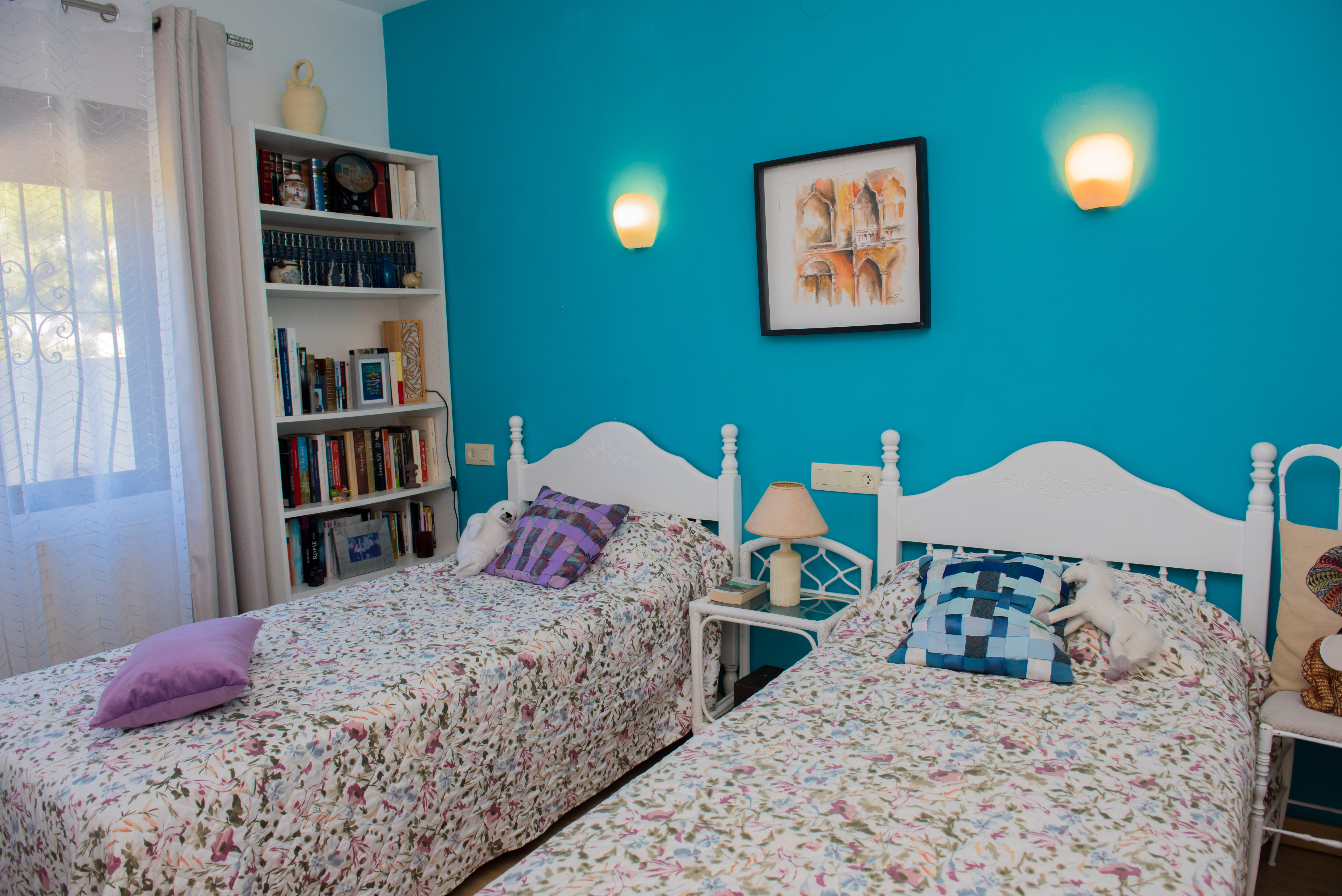 Schlafzimmer mit zwei Einzelbetten, türkisfarbener Wand und einem weißen Bücherregal.