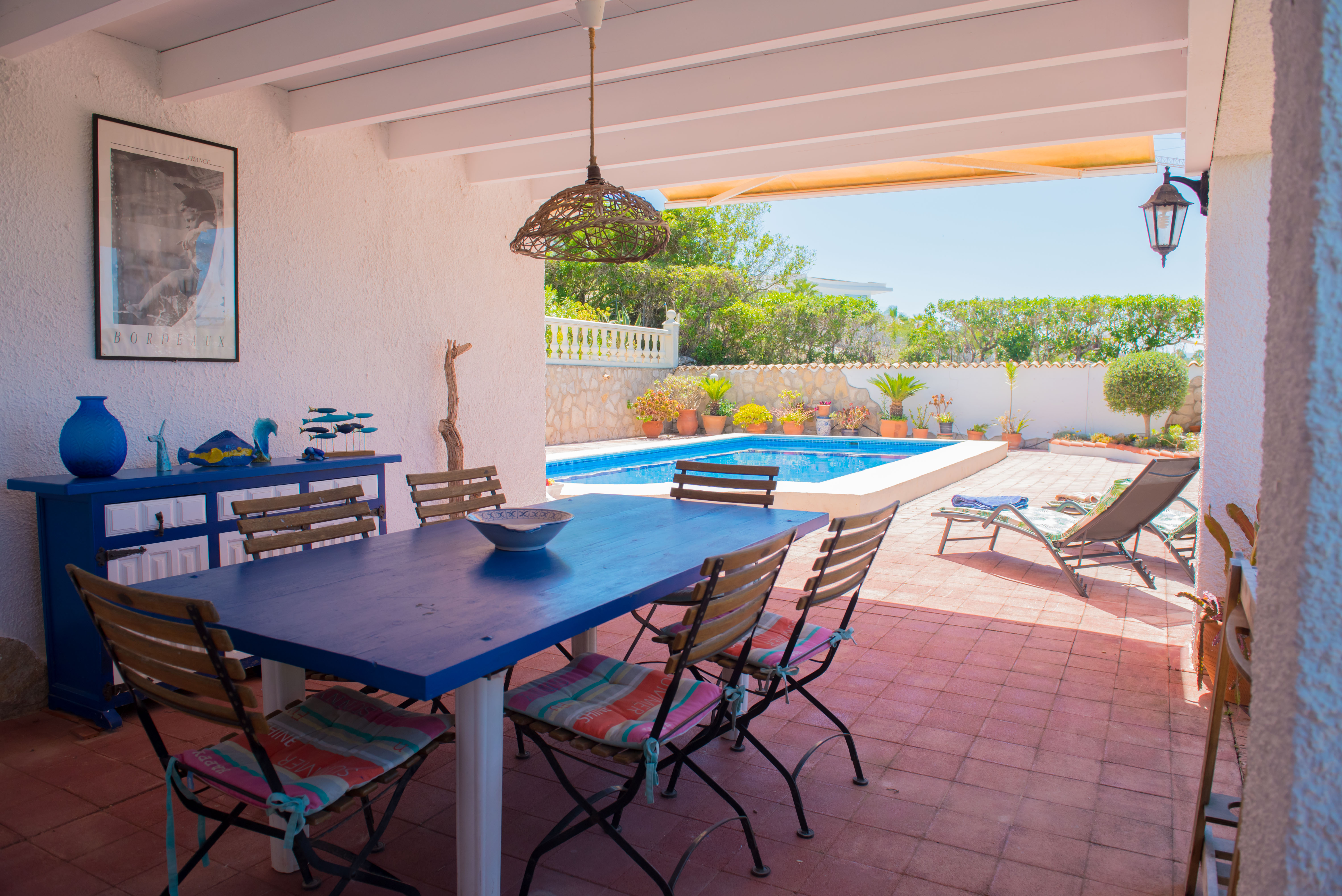 Überdachter Essbereich mit blauem Tisch und Poolblick.