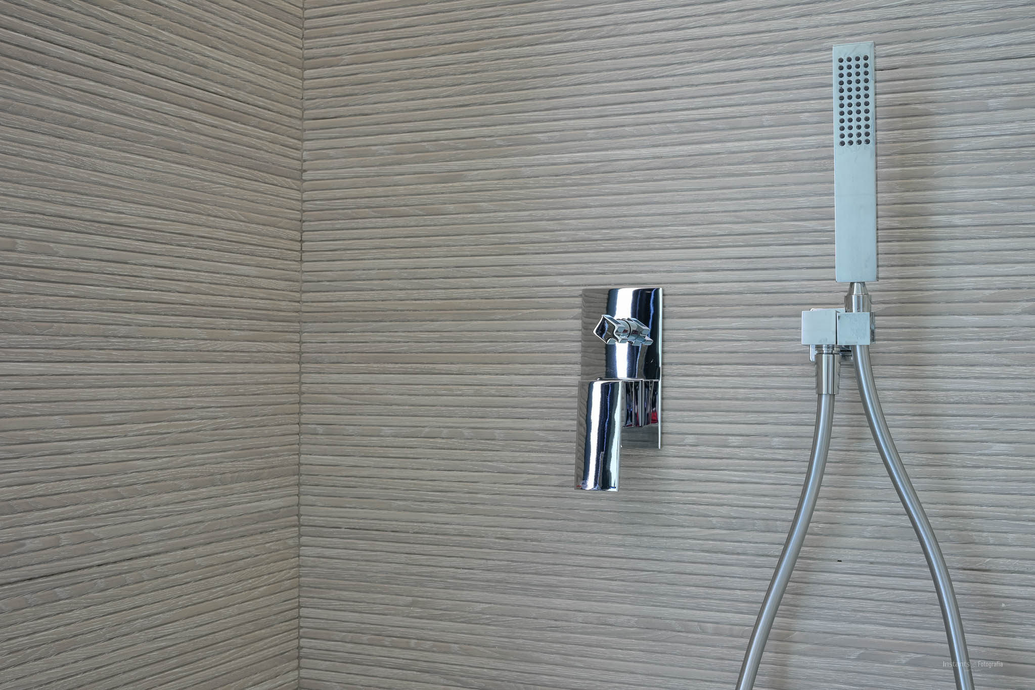 Duschbereich mit Chromarmatur und Handbrause vor einer Wand aus horizontal gerillten Strukturfliesen.