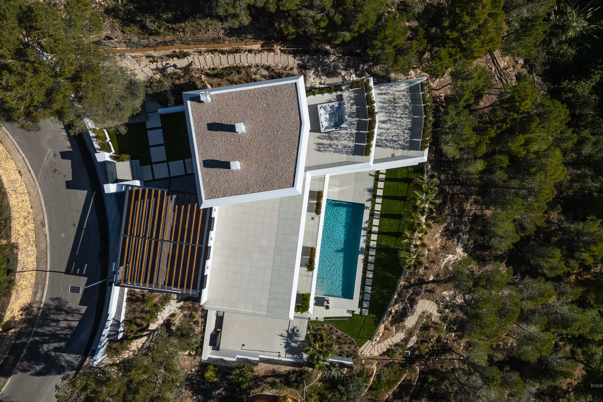 Luftaufnahme der modernen Villa mit rechteckigem Pool, weitläufigen gepflasterten Terrassen und einem Außen-Whirlpool, eingebettet in die natürliche mediterrane Landschaft.