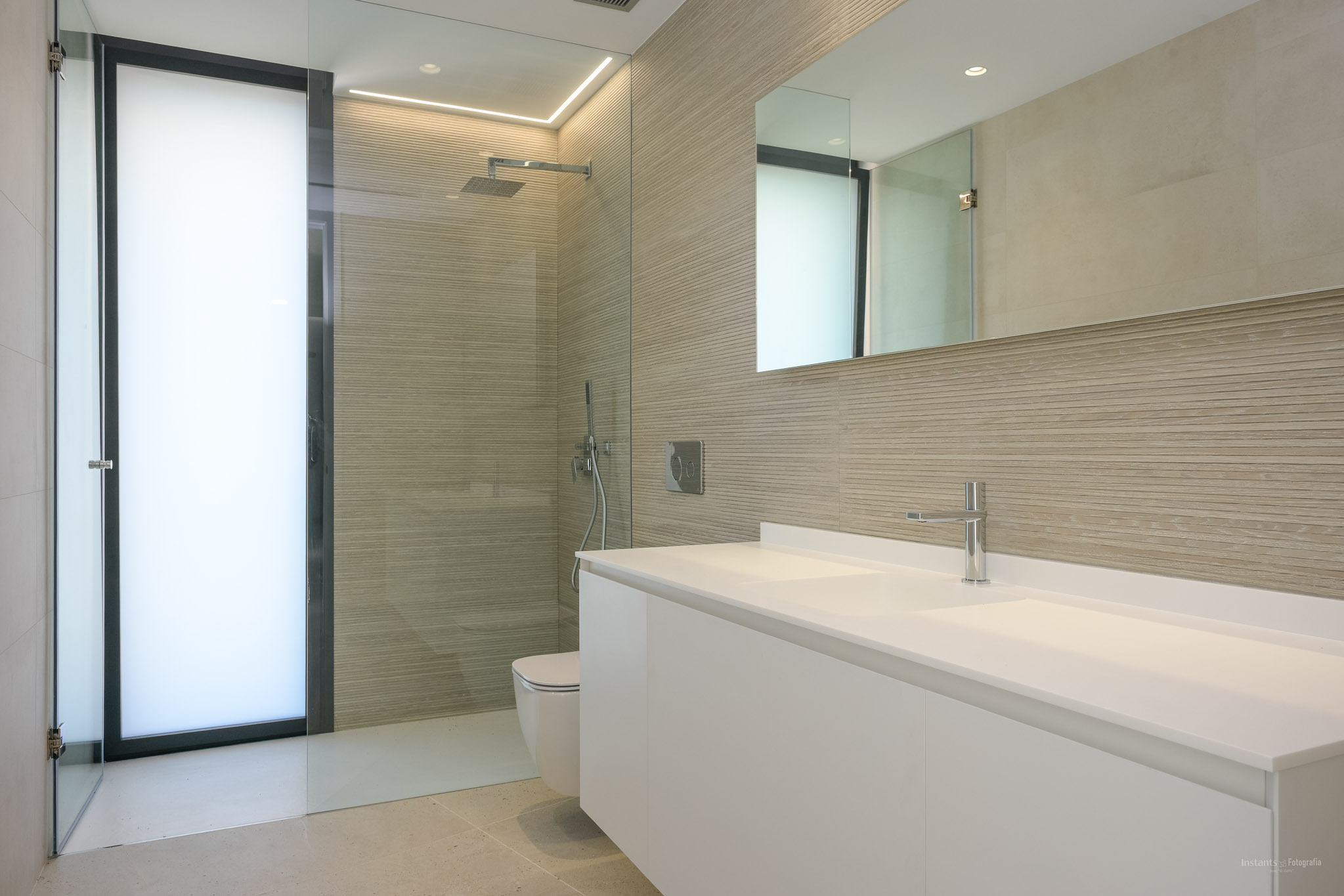 Modernes Badezimmer mit doppeltem schwebendem Waschtisch, begehbarer Dusche mit strukturierten Wandfliesen und Milchglastür, ergänzt durch Chromarmaturen und integrierte Beleuchtung.