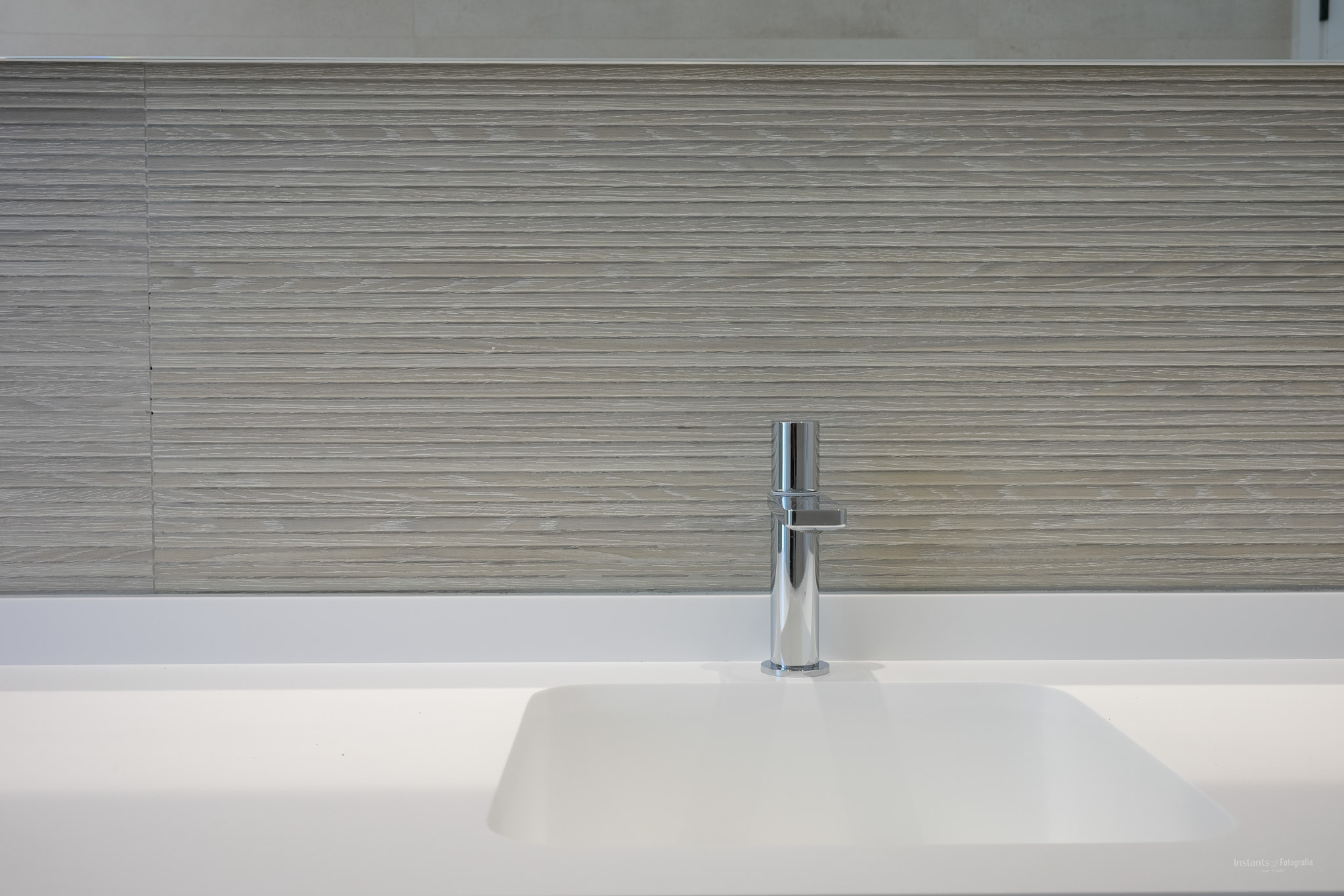 Modernes, integriertes weißes Waschbecken mit elegantem Chromarmatur. Die Wand ist mit hellen, horizontal strukturierten Fliesen verkleidet, die eine minimalistische Ästhetik schaffen.