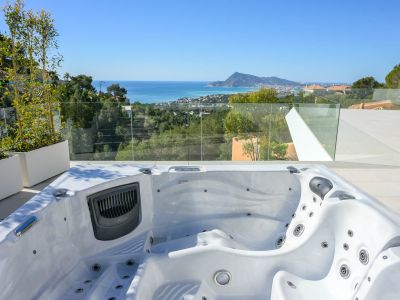Außen-Whirlpool auf gefliester Terrasse mit Panoramablick auf Mittelmeer, Küstenstadt und Berge. Glasgeländer und Pflanzen akzentuieren die Aussicht.