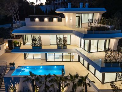 Die mehrstöckige moderne Architektur der Villa erstrahlt in der Dämmerung, mit einem leuchtend blauen Pool und weitläufigen Terrassen mit Glasgeländern.