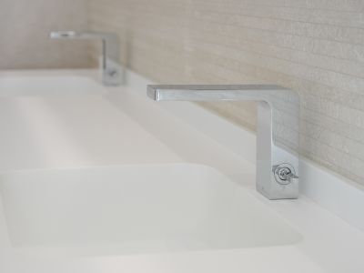 Doppelwaschtisch mit eleganten Chromarmaturen und integrierten weißen Waschbecken. Die Rückwand ist mit hellen, horizontal strukturierten Fliesen verkleidet.