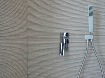 Duschbereich mit Chromarmatur und Handbrause vor einer Wand aus horizontal gerillten Strukturfliesen.