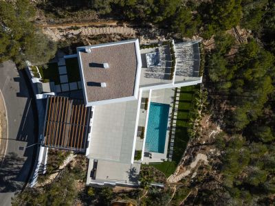 Luftaufnahme der modernen Villa mit rechteckigem Pool, weitläufigen gepflasterten Terrassen und einem Außen-Whirlpool, eingebettet in die natürliche mediterrane Landschaft.