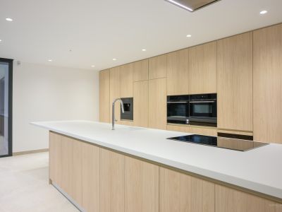Moderne Küche mit großer weißer Insel, integrierter Spüle und Induktionskochfeld, ergänzt durch raumhohe helle Holzschränke und Einbaubacköfen.