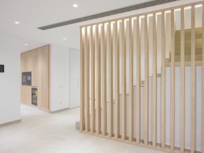 Moderner Innenraum mit heller Holzlamellenwand und integrierter Beleuchtung, die einen eleganten Küchenbereich mit Einbaugeräten von einer Steintreppe trennt.