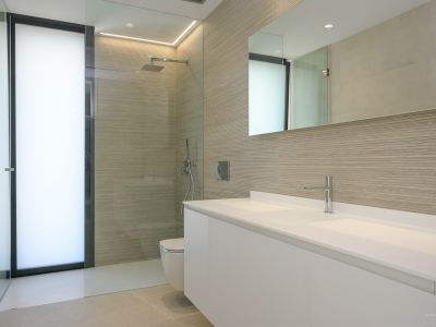 Modernes Badezimmer mit doppeltem schwebendem Waschtisch, begehbarer Dusche mit strukturierten Wandfliesen und Milchglastür, ergänzt durch Chromarmaturen und integrierte Beleuchtung.