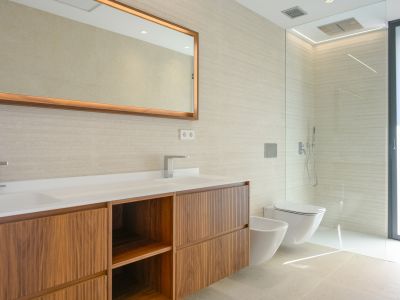 Modernes Badezimmer mit Doppelwaschtisch, Holzunterschränken und strukturierten Wandfliesen. Beleuchteter Spiegel, bodengleiche Dusche, wandhängendes WC und Bidet.
