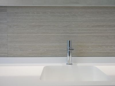 Modernes, integriertes weißes Waschbecken mit elegantem Chromarmatur. Die Wand ist mit hellen, horizontal strukturierten Fliesen verkleidet, die eine minimalistische Ästhetik schaffen.
